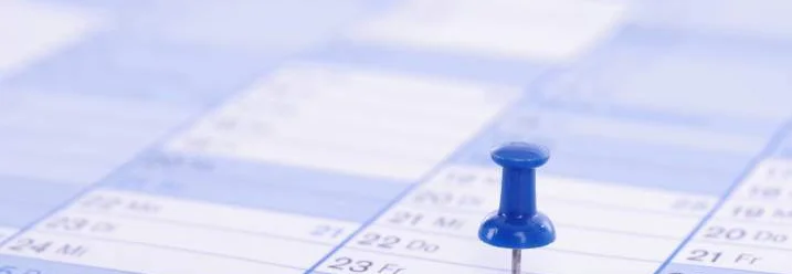 Ein blauer Pin markiert ein Datum auf einem Kalender.